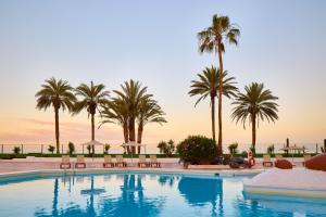 a swimming pool with palm trees and a sunset at SOL by Meliá Tenerife in Playa de las Americas