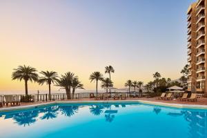 a large swimming pool with palm trees and the ocean at SOL by Meliá Tenerife in Playa de las Americas +16 photos