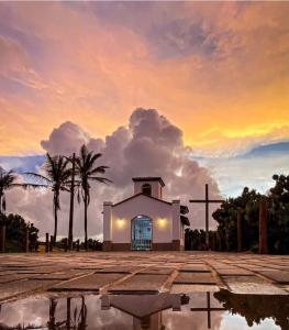 a church with a cross and palm trees and a sunset at Quarto privativo em Guriri casa de praia in São Mateus