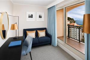 a room with a blue couch and a balcony at Columbus Hotel Monte-Carlo, Curio Collection by Hilton in Monte Carlo