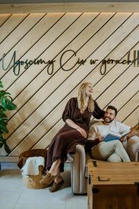 a man and woman sitting on a couch with a sign on a wall at Siedlisko Babia Góra in Zawoja