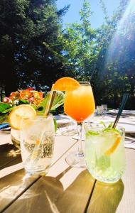 three glasses of drinks on a wooden table at Logis Hôtel Auberge de la Hulotte in Saint-Jacques-dʼAmbur