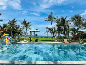 a swimming pool at a resort with palm trees and the ocean at The Vista Beach Resort Phan Thiết in Phan Thiet