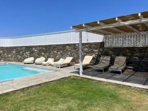 a swimming pool with lounge chairs and a stone wall at VIlla Gorgona, maison cycladique in Gavrio
