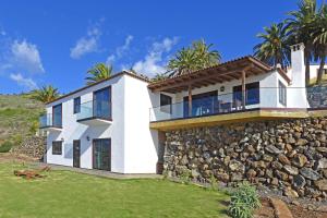 a white house with a stone wall and palm trees at Casa Vista Mar in Tijarafe