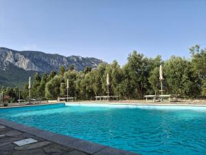 a swimming pool with picnic tables and mountains in the background at Agriturismo Palas De Serra Country Resort in Onifai