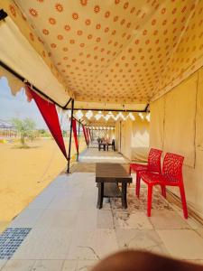 a tent with two red chairs and a wooden table at Big Brand Desert Camp in Jaisalmer