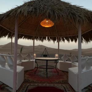 a room with a table and chairs under a straw umbrella at Best-Merzouga traditional camps in Merzouga