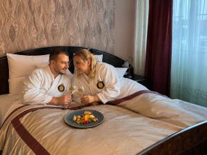a man and woman sitting on a bed with a plate of food at Hotel Rudolf in Hajdúszoboszló +74 photos