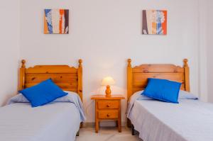 2 camas en un dormitorio con almohadas azules y lámpara en Apartamentos Carril de la Fuente, en Conil de la Frontera