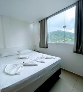 a bedroom with a bed with white sheets and a window at Princesa do Sertão Pousada in Palmeira dos Índios