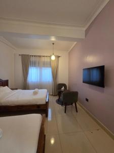 a bedroom with a bed and a tv and a chair at Paramount Boutique Hotel in Entebbe