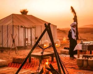 a man standing in front of a tent with a fire at Majestic Dunes Luxury Camp in Merzouga