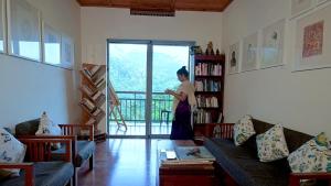 a woman standing in a living room with a book shelf at Mistletoe Munnar Homestay & Cafe in Munnar