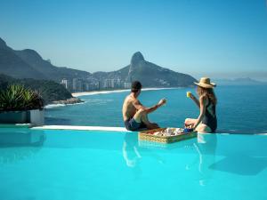 a man and woman sitting on the edge of a swimming pool at La Suite by Dussol in Rio de Janeiro