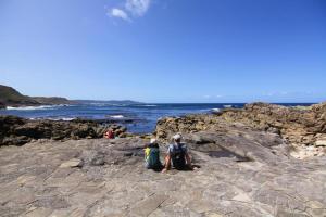 two people sitting on the rocks near the ocean at Casa dos Americanos - Suite Wellness in Briño