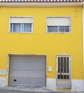 a yellow building with two garage doors and two windows at Casa da Maria in Amoreira