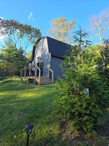 a gray house with a porch on a green field at Cozy Bethel Barn in Mongaup Valley