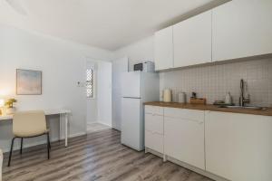 a kitchen with white cabinets and a table and a chair at Margate Beach Studio 4 in Redcliffe