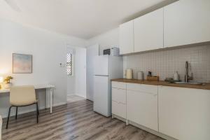a kitchen with white cabinets and a table and a chair at Margate Beach studio 2 in Redcliffe