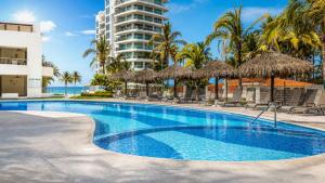 a swimming pool with straw umbrellas and the ocean at NITTA 209 Elegant Apartment - Partial Sea Views in Nuevo Nayarit