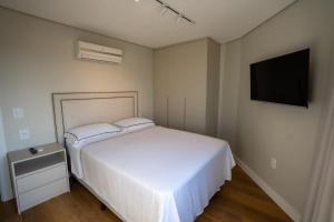 a bedroom with a white bed and a flat screen tv at Ap de novela no centro da cidade com garagem in Toledo