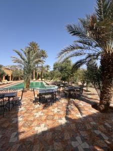 a patio with tables and chairs and palm trees at Riad Kasbah Le Touareg in Merzouga