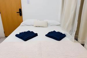 a white bed with two blue pillows on it at Abaíra Serra Azul Suítes 02 - Centro in Petrolina