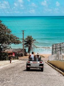 two people riding in a car down a road near the beach at Aura Mar Flat in Baía Formosa