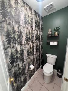 a bathroom with a toilet with a forest shower curtain at The Wandering Antler - Bragg Creek in Bragg Creek