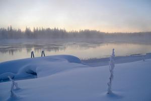 un grupo de personas de pie en la nieve junto a un cuerpo de agua en Peurasuvanto Mökit & Camping, en Peurasuvanto