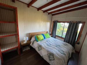 a bedroom with a bed with green pillows and a window at Cabañas Rayen Lemu in Panguipulli