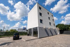 a white building with a car parked in a parking lot at NORTH GATE Rooms in Afumaţi