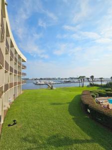 a building with a grassy yard next to a body of water at Salty Love Nest in Fort Walton Beach