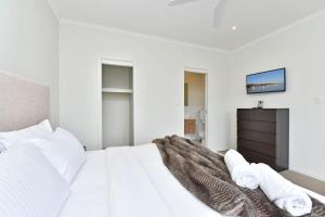 a white bedroom with a bed and a tv at Beach Escape at Caves Beach Villas in Caves Beach