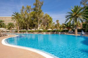 a large swimming pool with palm trees and umbrellas at SOL by Meliá Palmanova Mallorca in Palmanova