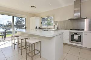 a white kitchen with a large counter and stools at Wangi Lakehouse in Wangi Wangi