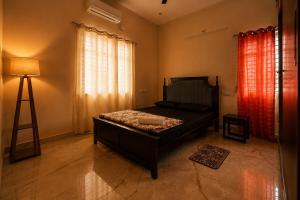 a bedroom with a bed and a lamp and curtains at Holapu Thayi Villa in Mysore