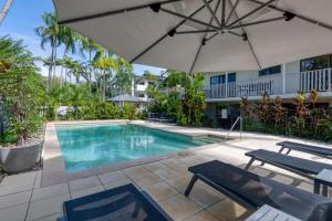 a swimming pool with an umbrella and two chairs at Seascape Holidays - Tropical Reef Apartments in Port Douglas