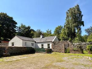 a white house with a stone wall and trees at Laundry Cottage in Strathpeffer