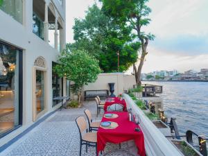 a table with red table cloths on a patio next to the water at Amdaeng Bangkok Riverside Hotel in Bangkok