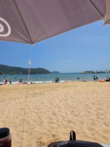 an umbrella on a beach with people in the water at Aju Good House 아주굿하우스 in Geoje