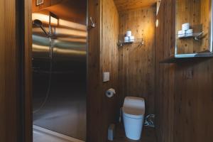 a bathroom with a toilet and a shower with wooden walls at Earthboat Ueda Onsen in Nagano