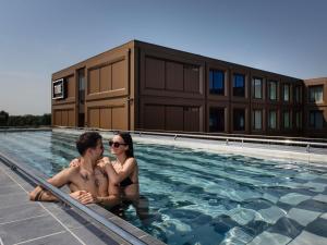 two people sitting in the water in a swimming pool at TRIBE Milano Malpensa in Vizzola Ticino