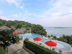 a swimming pool with red umbrellas and the ocean at Novotel Koh Si Chang in Ban Phanu Rangsi
