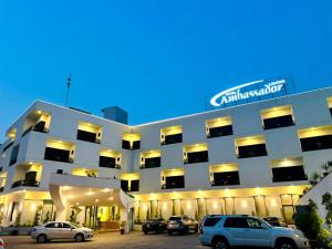 a large white building with cars parked in a parking lot at Ambassador Hotel in Lahore