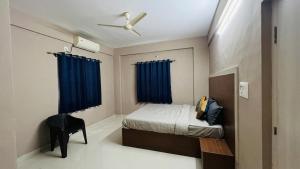 a bedroom with a bed and a chair and blue curtains at Fabhotel Aman palace in Mumbai