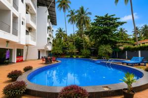a swimming pool in front of a building with palm trees at Sunlight Stay at Goa in Calangute