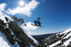 un hombre volando por el aire mientras monta una tabla de snowboard en Ski Club of Victoria - Kandahar Lodge en Mount Buller