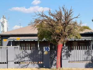 a tree in front of a building with a fence at Wampex Guesthouse in Potchefstroom +2 photos